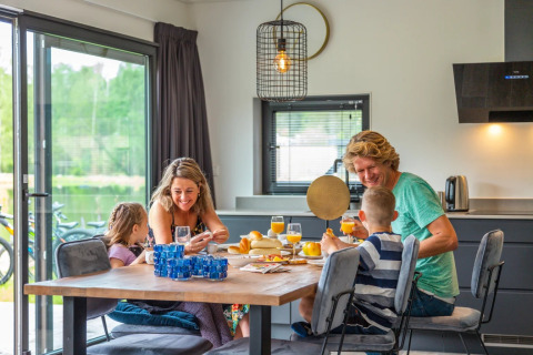 Gezin geniet van een ontbijt samen in een moderne glamping accommodatie met uitzicht op de natuur.
