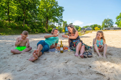 Gezin geniet van een picknick op een zandstrand met kinderen bij een vakantiepark met glamping.