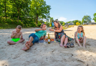 Gezin geniet van een picknick op een zandstrand met kinderen bij een vakantiepark met glamping.