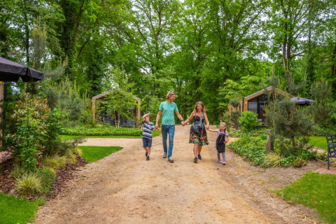 Gezin wandelt samen op een bospad bij een glamping vakantiepark met lodges en veel groene natuur.