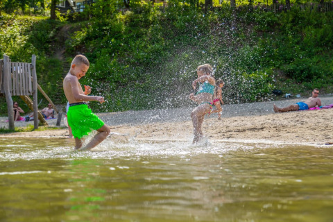 Kinderen spetteren water op een zonnig strand bij een vakantiepark met glampingaccommodaties.