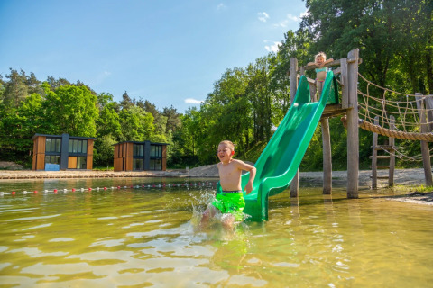 Kinderen spelen op een glijbaan in het meer bij een vakantiepark met moderne glampingaccommodaties.