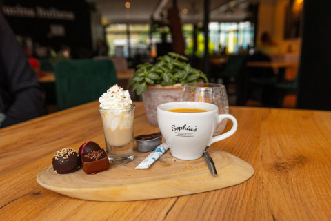 Een kop koffie, likeur met slagroom en pralines op een houten plank in een gezellig restaurant of café.
