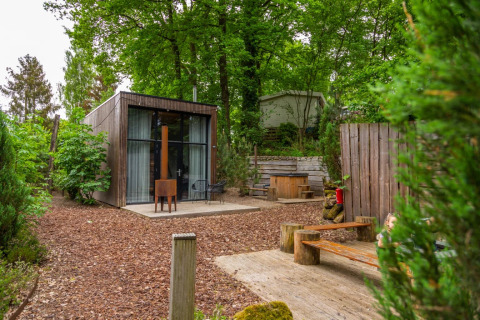 Glamping accommodatie in een vakantiepark met modern houten huisje, buitenzitjes en omgeven door groen.