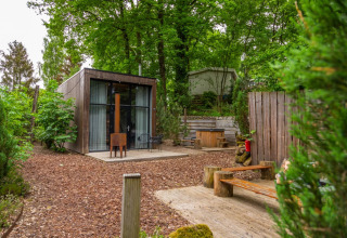 Glamping accommodatie in een vakantiepark met modern houten huisje, buitenzitjes en omgeven door groen.