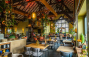 Gezellige eetruimte met houten plafond, veel planten en warme verlichting in een glamping vakantiepark.