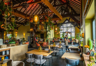 Gezellige eetruimte met houten plafond, veel planten en warme verlichting in een glamping vakantiepark.