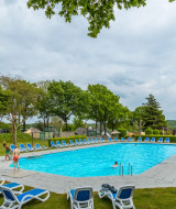 Buitenzwembad bij een vakantiepark met glampingaccommodaties, omringd door ligstoelen en groen.