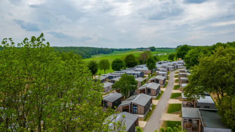 Luchtfoto van een vakantiepark met glampinghuisjes, omgeven door bomen en groene velden onder bewolkte hemel.