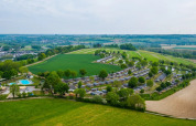 Luchtfoto van een vakantiepark met glamping accommodaties, chalets, zwembad en groene velden in België.