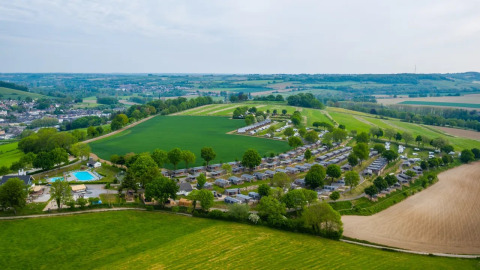 Luchtfoto van een vakantiepark met glamping accommodaties, chalets, zwembad en groene velden in België.