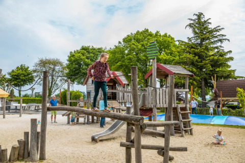 Kinderen spelen op een houten speeltoestel in een speeltuin bij een vakantiepark met glamping.