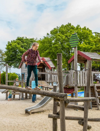 Kinderen spelen op een houten speeltoestel in een speeltuin bij een vakantiepark met glamping.