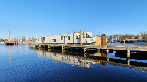 El barco casa Houseboat De Zwerver amarrado en Marina Parcs Naarden, Países Bajos, en un día soleado.