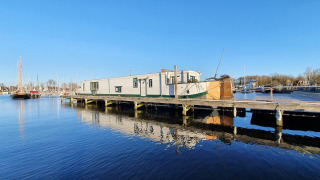 El barco casa Houseboat De Zwerver amarrado en Marina Parcs Naarden, Países Bajos, en un día soleado.