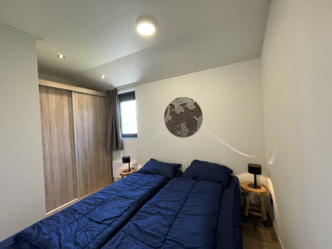Slaapkamer in een tiny house met twee aparte bedden, blauwe dekens en een houten kast.