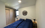 Slaapkamer in een tiny house met twee aparte bedden, blauwe dekens en een houten kast.