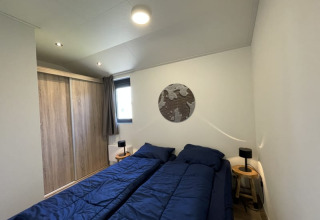 Dormitorio en una tiny house con dos camas individuales, ropa de cama azul y armario de madera.