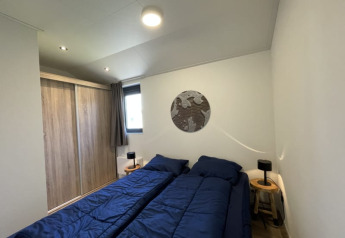 Soveværelse i et tiny house med to enkeltsenge, blå dyner, natborde og garderobeskab.