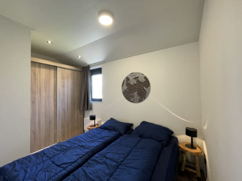 Modern tiny house slaapkamer met twee eenpersoonsbedden, blauwe dekbedden en houten nachtkastjes.