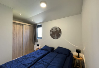 Camera moderna in una tiny house, due letti singoli con piumini blu e armadio in legno chiaro.
