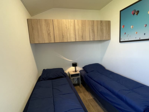 Dormitorio en una tiny house con dos camas individuales, ropa de cama azul, armarios y una mesita.