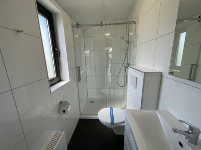 Baño moderno y pequeño en una tiny house con ducha, inodoro, lavabo y una ventana que deja pasar la luz.