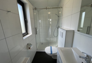 Moderne, lille badeværelse i et tiny house med bruseniche, toilet, håndvask og et vindue med dagslys.