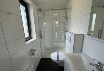 Petite salle de bain moderne dans une tiny house avec douche, toilettes, lavabo et fenêtre lumineuse.