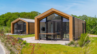 Zwei moderne Tiny Houses mit Holzfassade und großen Fenstern stehen in einer grünen, sonnigen Landschaft.