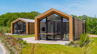 Zwei moderne Tiny Houses mit Holzfassade und großen Fenstern stehen in einer grünen, sonnigen Landschaft.