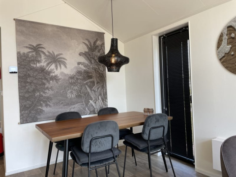 Moderne eethoek in een tiny house met houten tafel, vier stoelen, zwarte lamp en natuurwandtapijt.