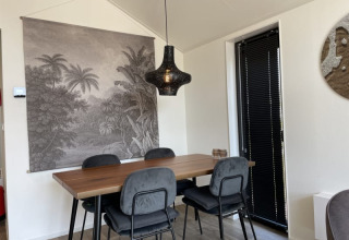Comedor moderno en una tiny house con mesa de madera, cuatro sillas, lámpara negra y tapiz de paisaje.