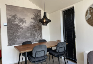 Moderne eethoek in een tiny house met houten tafel, vier stoelen, zwarte lamp en natuurwandtapijt.