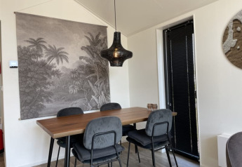 Zona pranzo moderna in una tiny house con tavolo in legno, quattro sedie e arazzo da parete paesaggistico.