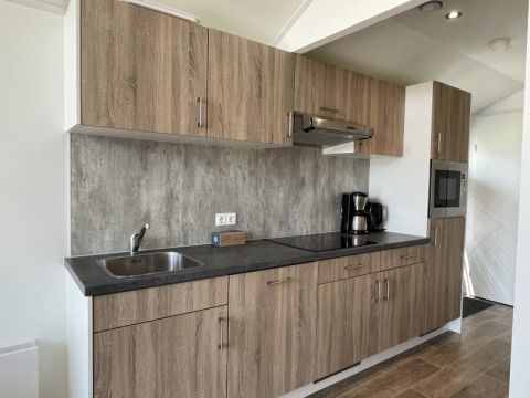 Cucina moderna di una tiny house con mobili in legno, lavello, piano cottura e macchina del caffè.