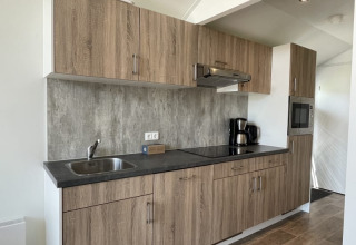 Cucina moderna di una tiny house con mobili in legno, lavello, piano cottura e macchina del caffè.