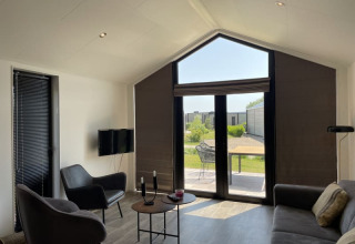 Sala minimalista en una tiny house con grandes ventanales, muebles modernos y vista al jardín exterior.