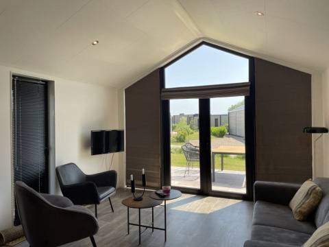 Minimalistisk stue i et tiny house med store vinduer, moderne møbler og udsigt til en have udenfor.