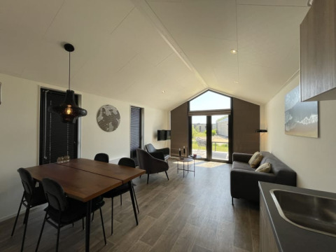 Interior moderno y luminoso de tiny house con mesa de comedor, sofá y ventanales hacia el jardín.
