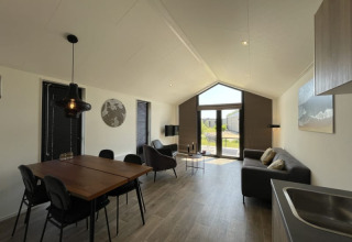 Modernes, helles Tiny House mit Esstisch, Sofa, großen Fenstern und Blick auf den Garten.