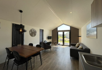 Modernes, helles Tiny House mit Esstisch, Sofa, großen Fenstern und Blick auf den Garten.