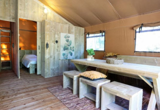 Intérieur d’un lodge moderne avec mobilier en bois, grande table, bancs et lumière naturelle des fenêtres.