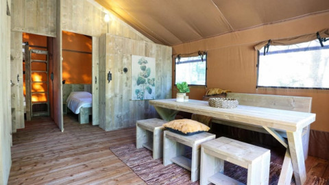 Interior de una moderna cabaña de madera con mesa grande, bancos y luz natural que entra por las ventanas.