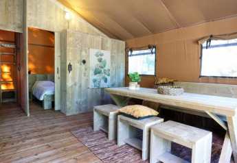 Interior de una moderna cabaña de madera con mesa grande, bancos y luz natural que entra por las ventanas.