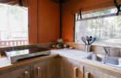 Rincón de cocina moderno en una cabaña con placa de inducción, fregadero y vistas al bosque por las ventanas.