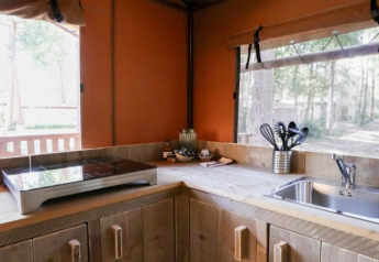 Rincón de cocina moderno en una cabaña con placa de inducción, fregadero y vistas al bosque por las ventanas.