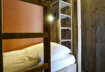 A cozy lodge room featuring a wooden bunk bed, ladder, soft white bedding, and gentle warm lighting.