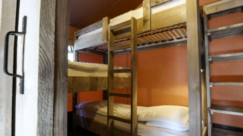 Et hyggeligt værelse på en lodge med køjesenge i træ, rene hvide puder og orange vægge.