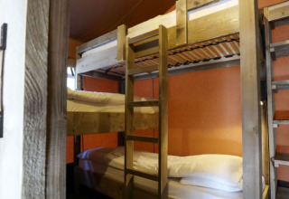 Habitación acogedora en una cabaña con literas de madera, almohadas blancas y paredes color naranja.